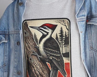 May include: A grey t-shirt with a vintage-style illustration of a woodpecker perched on a tree branch. The illustration is surrounded by a red, white, and blue border.