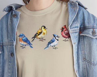 May include: A beige t-shirt with a colorful bird design. The birds are a bluebird, a yellow bird, a blue jay, and a cardinal.