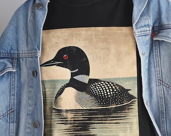 May include: A black t-shirt featuring a vintage-style illustration of a loon swimming in water. The loon has black and white feathers and red eyes.