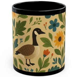 May include: A black-handled coffee mug with a beige background featuring a goose illustration and colorful floral patterns. The goose is brown, beige, and black. The flowers are blue, orange, and yellow. The mug is a standard 11 oz size.
