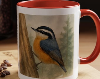Puede incluir: Una taza de cerámica blanca con un borde y un asa rojos. La taza presenta una ilustración de acuarela de un pájaro azul grisáceo con marcas naranja y blancas posado en una rama de árbol. El fondo es una acuarela de verde y marrón.