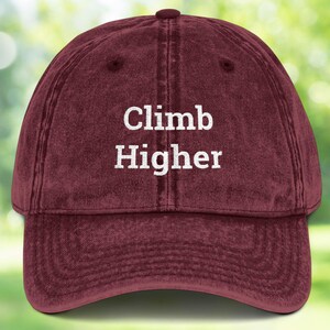 May include: A maroon vintage-style baseball cap with the text "Climb Higher" embroidered in white on the front.