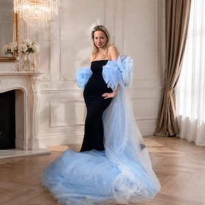 May include: A floor-length black strapless gown featuring voluminous, detachable light blue tulle sleeves that extend into a long, flowing train. The bodice is fitted and solid black, contrasting with the sheer, layered texture of the blue tulle.