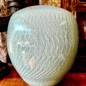 May include: A large, round, green ceramic vase with a crackled glaze. The vase has a light blue and gold paint design.