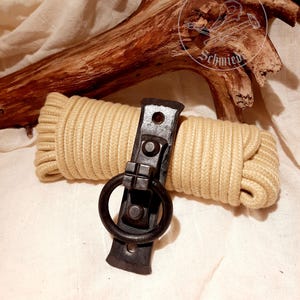 May include: A black metal door handle with a ring pull. The handle is mounted on a wooden board. The board is resting on a beige fabric surface. The text "Dohlen Schmied" is visible in the background.