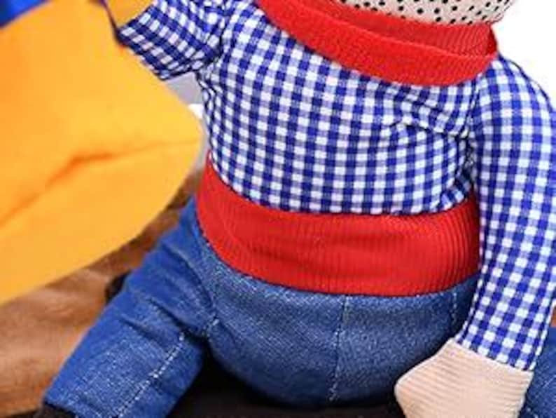 May include: A plush toy monkey wearing a blue and white checkered shirt, red pants, and a red belt.