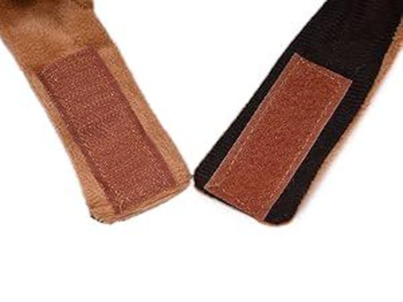 May include: Close-up of two brown faux fur straps with brown hook and loop fasteners. The straps are attached to a black fabric.