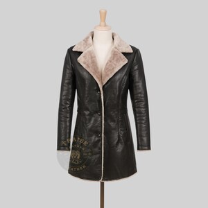 May include: A black leather coat with a beige faux fur collar and lining, displayed on a mannequin. The coat has a button-down front and a tailored fit. The coat is a mid-length style.