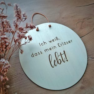 Könnte beinhalten: Runder, hellfarbiger Holzschild mit dem deutschen Text "Ich weiß, dass mein Erlöser lebt!" in dunkelbrauner Schrift. Das Schild hat eine braune Lederschlaufe zum Aufhängen.