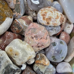 May include: A collection of polished gemstones in various shapes and sizes. The stones display a range of colors, including white, gray, brown, and pink, with unique patterns and textures. The gemstones are smooth and appear to be tumbled.