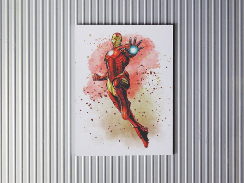 Puede incluir: Una pintura de acuarela de Iron Man volando por el aire con un traje rojo y dorado. El fondo es una acuarela roja y amarilla.