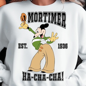 May include: White sweatshirt featuring a cartoon character named Mortimer in a green and tan outfit. The design includes the name "MORTIMER" above the character, with "EST. 1936" and "HA-CHA-CHA!" also printed on the sweatshirt.
