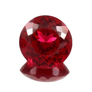 May include: A round, faceted gemstone with a deep, vibrant red color. The stone features a complex geometric cut that creates multiple light-reflecting surfaces, resulting in a brilliant, sparkling appearance against a plain white background.
