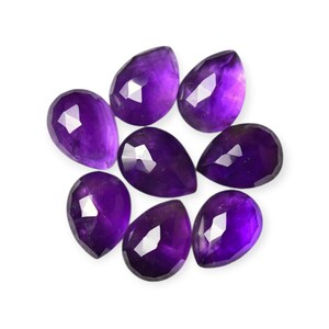 May include: Eight faceted, teardrop-shaped amethyst gemstones. The gemstones are a deep purple color with reflective surfaces, arranged against a white background. These gemstones are suitable for jewelry making or collecting.