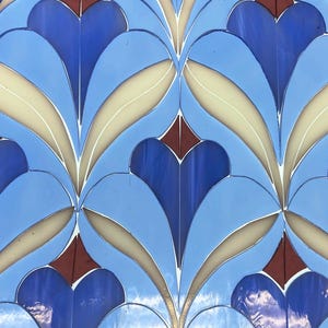 May include: A close-up of a stained glass design featuring a repeating pattern of blue, light blue, cream, and maroon shapes. The design is reminiscent of Art Deco or Art Nouveau styles. The word "cricut" is visible at the bottom.