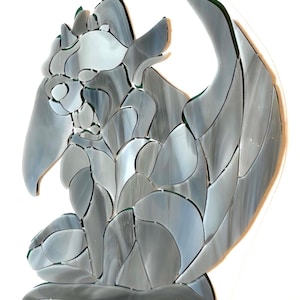 May include: A mosaic artwork depicting a gargoyle in shades of gray and white. The sculpture features a detailed wing, a beak, and a seated pose. The mosaic is made of irregular pieces of glass, creating a textured effect.