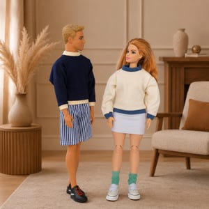 Op de afbeelding: Twee poppen staan naast elkaar. De pop aan de linkerkant heeft blond haar, een marineblauwe trui met lange mouwen en witte boorden, een blauw-wit gestreepte korte broek en zwarte sneakers. De pop aan de rechterkant heeft lang rood haar, een cr&egrave;mekleurige trui met blauwe boorden, een witte rok, groene sokken en witte sneakers.