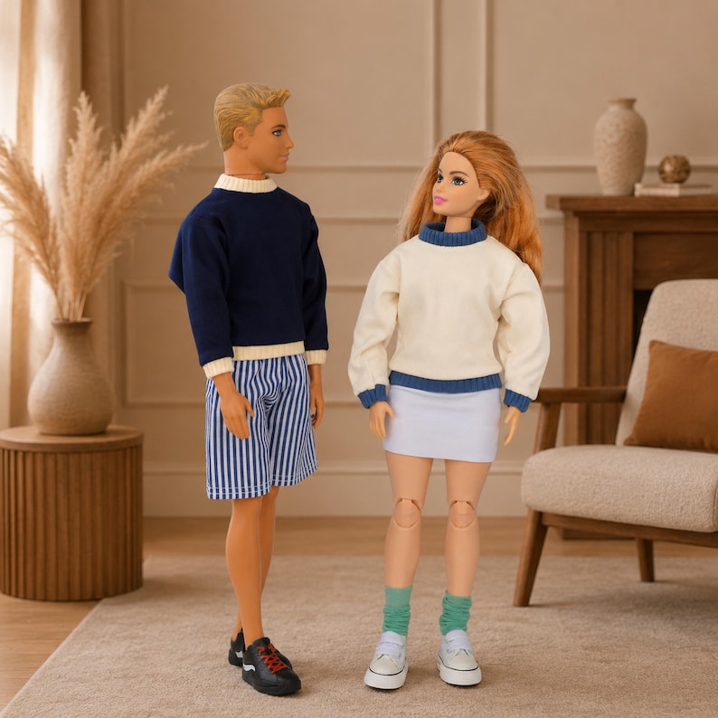 Op de afbeelding: Twee poppen staan naast elkaar. De pop aan de linkerkant heeft blond haar, een marineblauwe trui met lange mouwen en witte boorden, een blauw-wit gestreepte korte broek en zwarte sneakers. De pop aan de rechterkant heeft lang rood haar, een cr&egrave;mekleurige trui met blauwe boorden, een witte rok, groene sokken en witte sneakers.