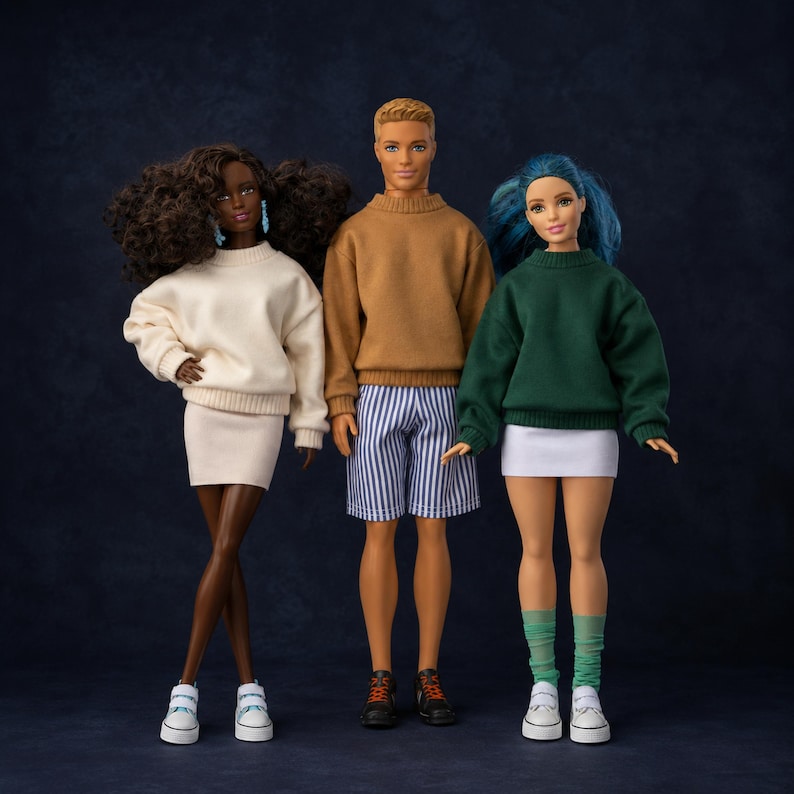 Op de afbeelding: Drie poppen staan bij elkaar. De linkerpop heeft donker krullend haar en draagt een cr&egrave;mekleurige trui en rok met witte sneakers. De middelste pop heeft kort blond haar, een beige trui, blauw-wit gestreepte shorts en zwarte sneakers. De rechterpop heeft blauw haar, een groene trui, een witte rok en witte sneakers.