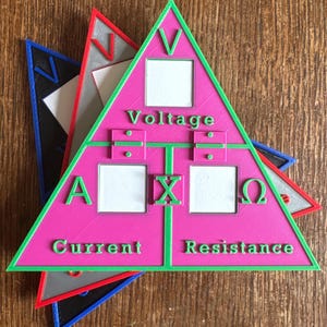 Puede incluir: Un triángulo rosa, verde y blanco impreso en 3D con la palabra "Voltage" en la parte superior y "Current" y "Resistance" en la parte inferior. El triángulo tiene un borde verde e incluye símbolos matemáticos y letras. Se ven otros triángulos en azul, rojo y gris.