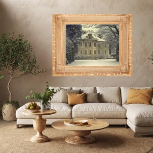 May include: A rectangular wall art piece featuring a landscape painting of a large manor house surrounded by snow-covered trees and grounds, enclosed within an ornate, wide, light-colored wooden frame with carved decorative detailing.