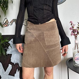 May include: Black zip-up top with sheer striped sleeves and a brown suede mini skirt. The top has a collared neckline. The skirt features a pocket and a patchwork design.