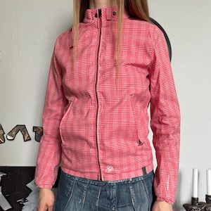 May include: A red and white plaid jacket with a zipper closure and a small logo on the chest. The jacket is paired with a denim skirt. The jacket has a hood and pockets.