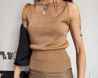 May include: A sleeveless, tan-colored knit top with a keyhole detail at the neckline. The top is paired with matching tan pants. A black handbag with a bamboo handle hangs on the left side. Accessories include a silver choker and a wide cuff bracelet.