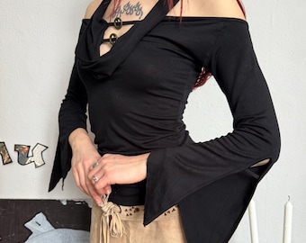 May include: Black off-the-shoulder top with long, flared sleeves. The top features a halter neckline with decorative buttons. Paired with a tan suede mini skirt with a tie waist. A stylish ensemble.