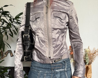 May include: A silver-gray satin jacket with a zip-up front, two chest pockets, and a belted waist. Paired with a denim mini skirt and a black shoulder bag. The jacket has a high collar and long sleeves.