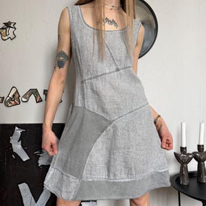 May include: A sleeveless gray dress with a patchwork design. The dress features a square neckline and a flared skirt. The fabric appears to be linen or a similar textured material. The dress is knee-length and has a casual, bohemian style.