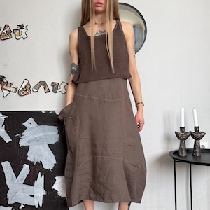 May include: A brown two-piece outfit, comprising a tank top and a midi skirt. The tank top is a darker shade of brown, contrasting with the lighter skirt. The outfit is worn with black sandals. The fabric appears soft and flowing.