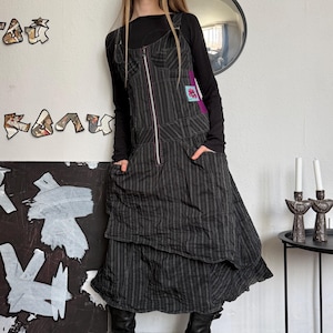 May include: A black and gray striped dress with a zipper front and pockets. The dress is layered and worn over a black long-sleeve shirt. The model is wearing black boots.