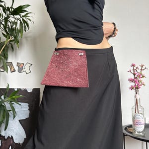 May include: A black skirt with a burgundy pocket. The skirt is long and flowing, with a simple design. The pocket is rectangular and textured. The model is wearing a black top.