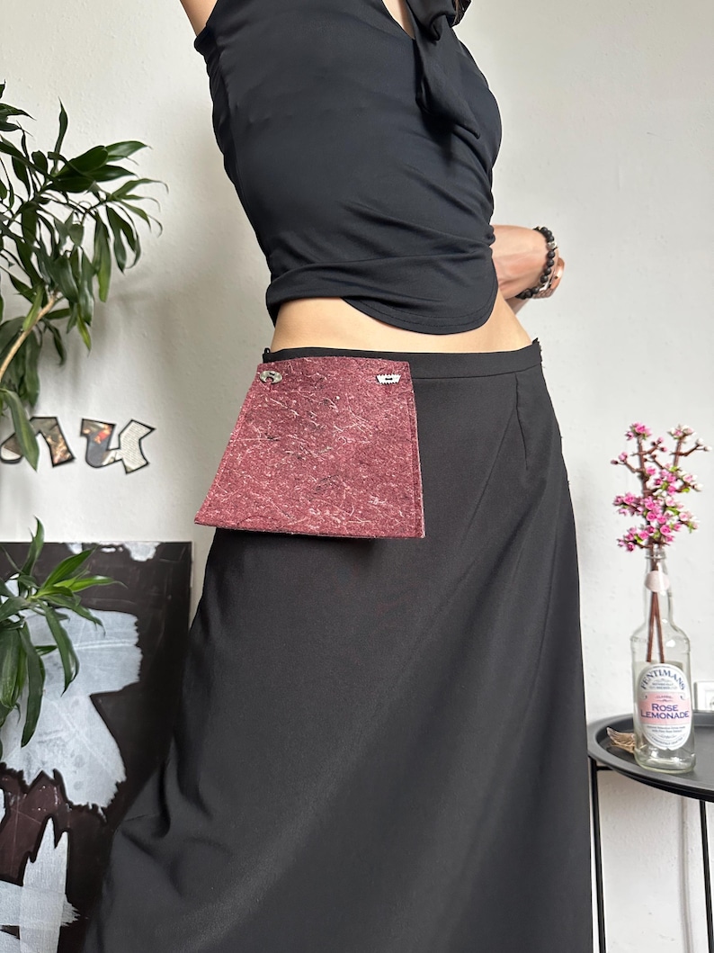 May include: A black skirt with a burgundy pocket. The skirt is long and flowing, with a simple design. The pocket is rectangular and textured. The model is wearing a black top.