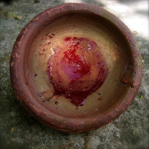 Puede incluir: Un cuenco de terracota con un líquido rojo en su interior. El cuenco tiene un esmalte de color dorado y está ligeramente astillado.