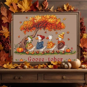 May include: A framed cross-stitch featuring four geese in autumn attire walking under a tree with falling leaves. The artwork is surrounded by fall foliage and pumpkins, with the word "Goose-tober" at the bottom.