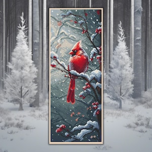 Könnte beinhalten: Ein gerahmtes Kreuzstichbild eines roten Kardinals, der auf einem schneebedeckten Ast mit roten Beeren sitzt. Der Hintergrund ist eine verschneite Waldszene mit weißen Bäumen und einem hellgrauen Himmel. Das Kunstwerk ist rechteckig und hat einen beigen Rahmen.