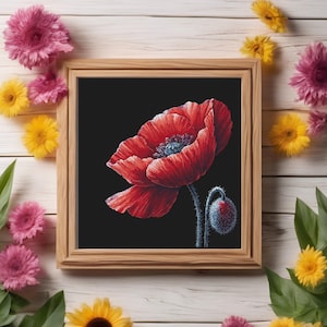 Puede incluir: Una bordadura de punto de cruz enmarcada de una flor de amapola roja sobre un fondo negro. El marco es de madera y tiene un acabado natural. La amapola está en flor y tiene un capullo.