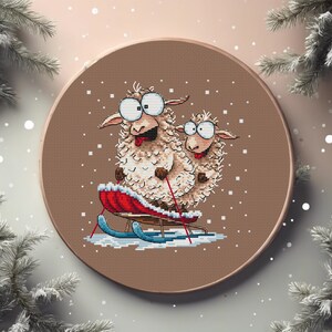 May include: Cross-stitch embroidery of two sheep on a sled, set against a brown background. The sheep have large, expressive eyes and are smiling. The sled is red with blue runners, and the scene is set in a snowy environment, with snowflakes falling.