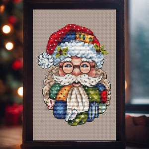 May include: Cross-stitch artwork of Santa Claus in a wooden frame. Santa is depicted with a red hat, white beard, and glasses. His outfit is a patchwork of colorful fabrics. The background is a neutral tan color.