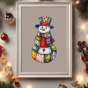 Pode incluir: Um ponto de cruz emoldurado de um boneco de neve. O boneco de neve tem um chap&eacute;u azul, um nariz de cenoura e um cachecol colorido. O corpo &eacute; feito de quadrados de patchwork em v&aacute;rias cores e padr&otilde;es. A moldura &eacute; branca.