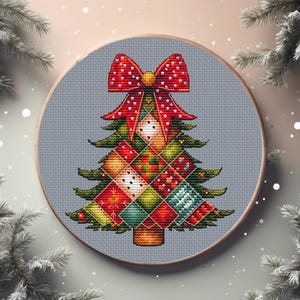 Peut inclure: Une broderie au point de croix représentant un sapin de Noël dans un cercle à broder en bois. L'arbre est composé de carrés colorés à motifs et surmonté d'un nœud rouge à pois blancs. Le fond est en tissu gris clair.
