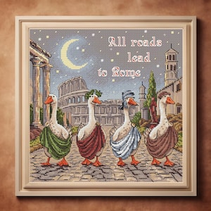 Puede incluir: Obra de arte de punto de cruz enmarcada que representa a cuatro gansos vestidos a la romana caminando por un camino empedrado. El fondo presenta arquitectura romana, una luna creciente y el texto "All roads lead to Rome."