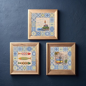 May include: Three framed cross-stitch artworks. One shows a lighthouse, another three colourful fish, and the third a yellow tram with the word "Lisbon". Each artwork is surrounded by a blue and white tile pattern.