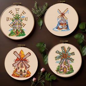 May include: Four cross-stitch windmill designs in wooden hoops. Each features a unique color palette and style, including a winter scene with snow and ice, and a fall scene with pumpkins. The windmills have detailed cross-stitch patterns.