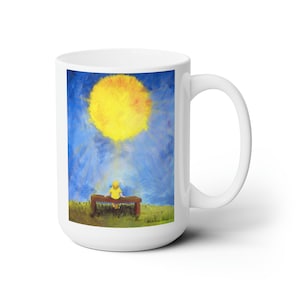 May include: White ceramic mug with a colorful painting of a child sitting on a bench looking up at a large yellow sun in a blue sky.
