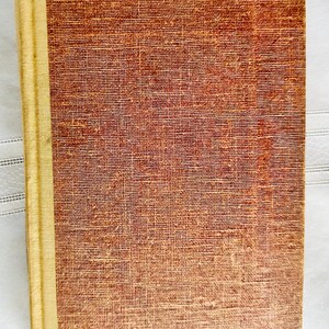 May include: A vintage hardcover book with a brown cover and a gold spine. The cover has a textured fabric pattern.