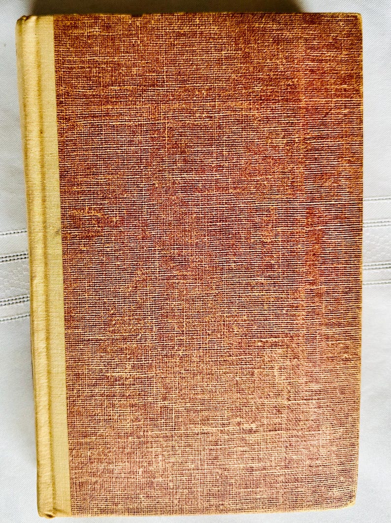 May include: A vintage hardcover book with a brown cover and a gold spine. The cover has a textured fabric pattern.