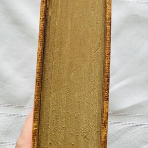 May include: Close-up of the spine of a vintage, hardback book with a brown leather cover and gold-colored edging. The book is worn and has a slightly faded appearance.